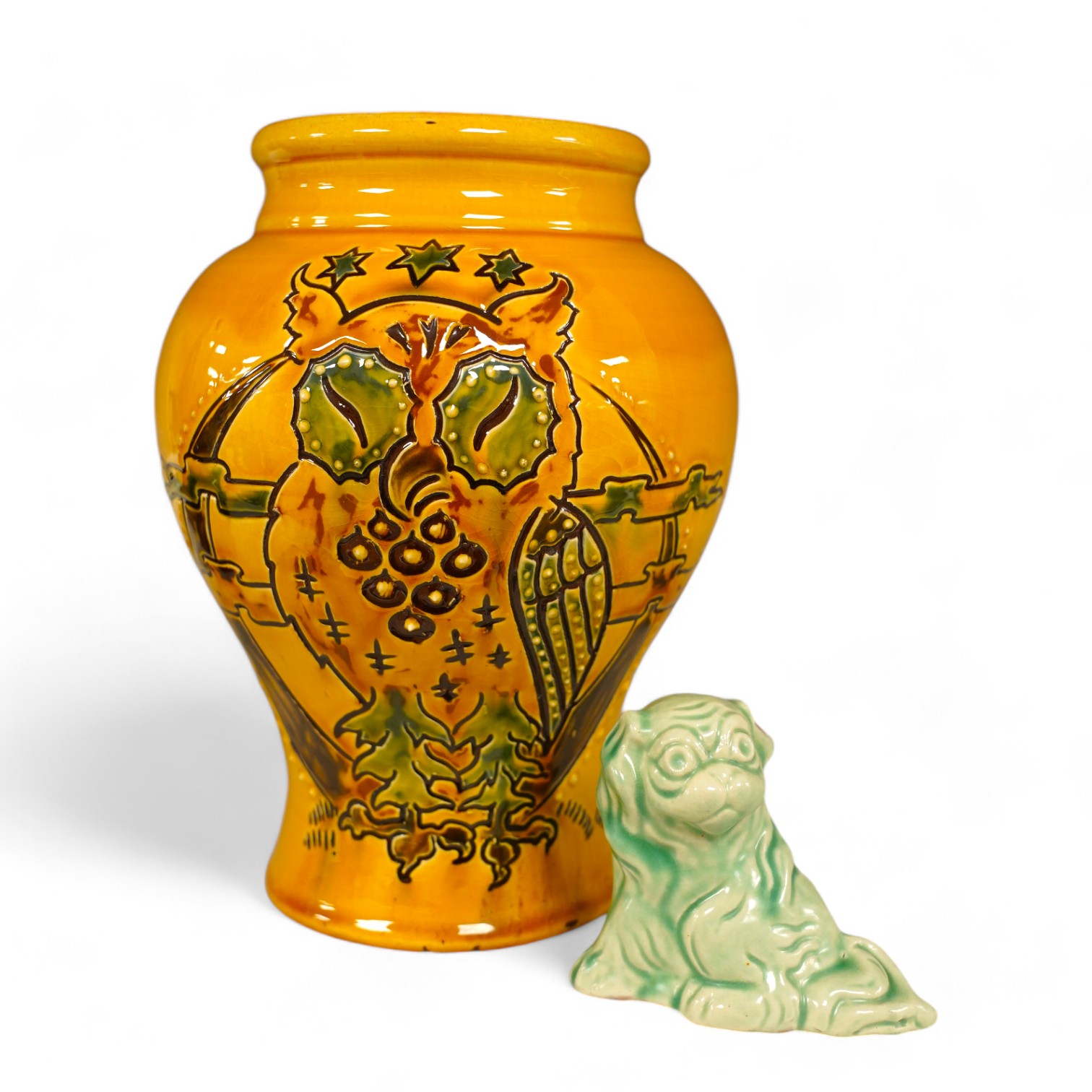 A Brannam yellow vase with stylised decoration of a standing owl with a background of the moon, clouds and three stars, 21cm high, and a Brannam, Barnstaple, a shade of green stylised sitting Dog of Fo, 7.5cm high. Condi